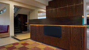 A reception area with a wooden reception desk, a black screen, and a colorful carpet. - Fabhotel Seven Elite (Paud)
