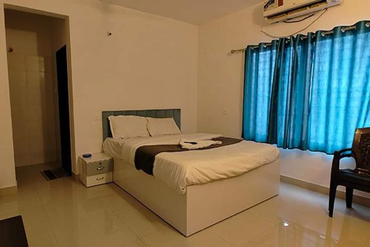 A hotel room with a bed, a bedside table, a chair, and a window with curtains.