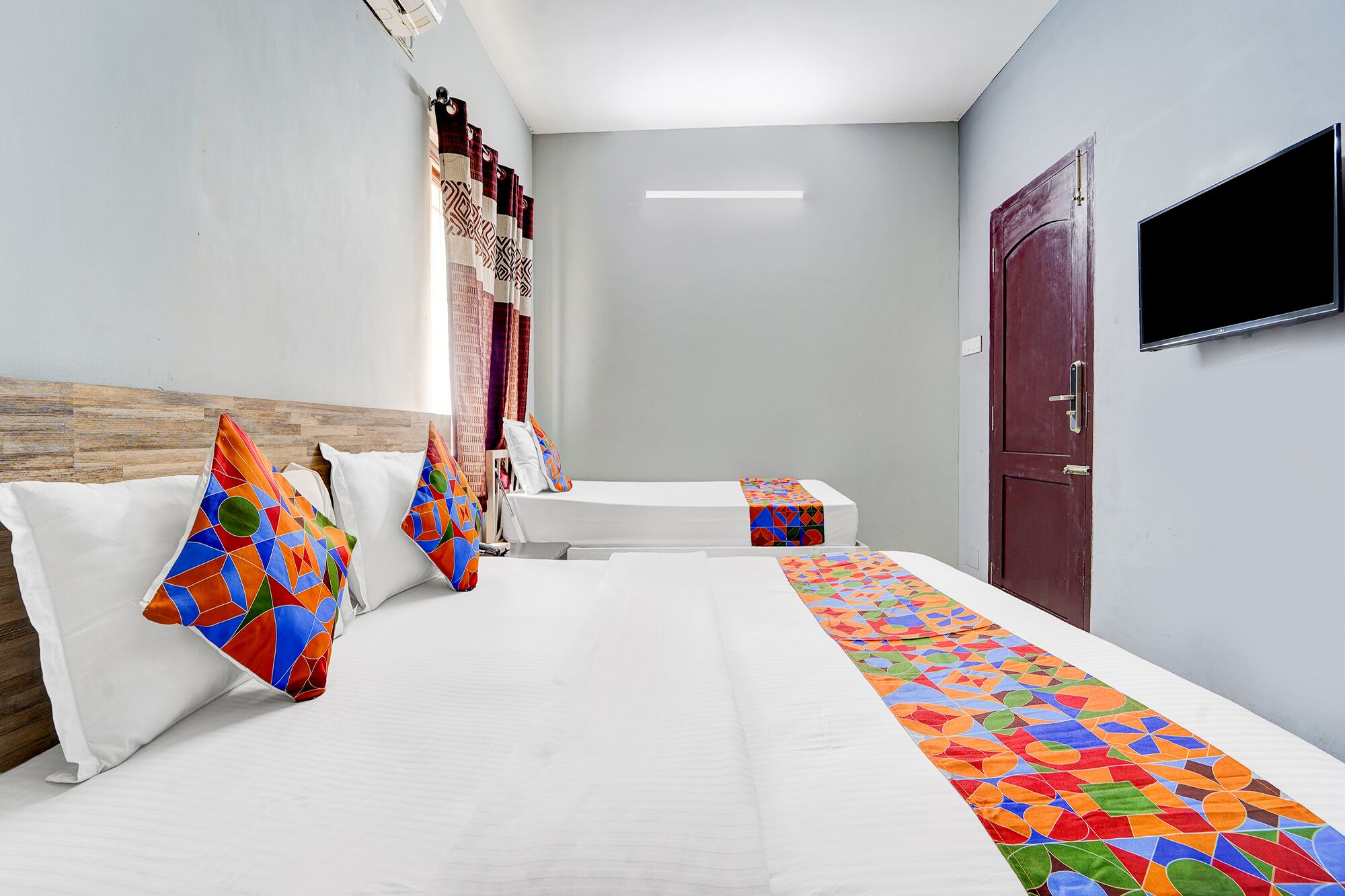 Een hotelkamer met een groot bed, twee nachtkastjes, een aan de muur bevestigde televisie en een deur.