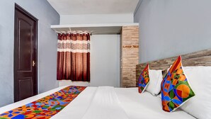 Ein Hotelzimmer mit Bett, einem Fenster mit gemusterten Vorhängen und einem Kopfteil mit dekorativen Kissen.