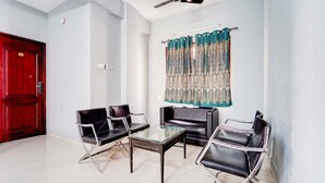 Ein Zimmer mit einer roten Tür, zwei schwarzen Ledersesseln, einem Glastisch und einem gemusterten Vorhang.