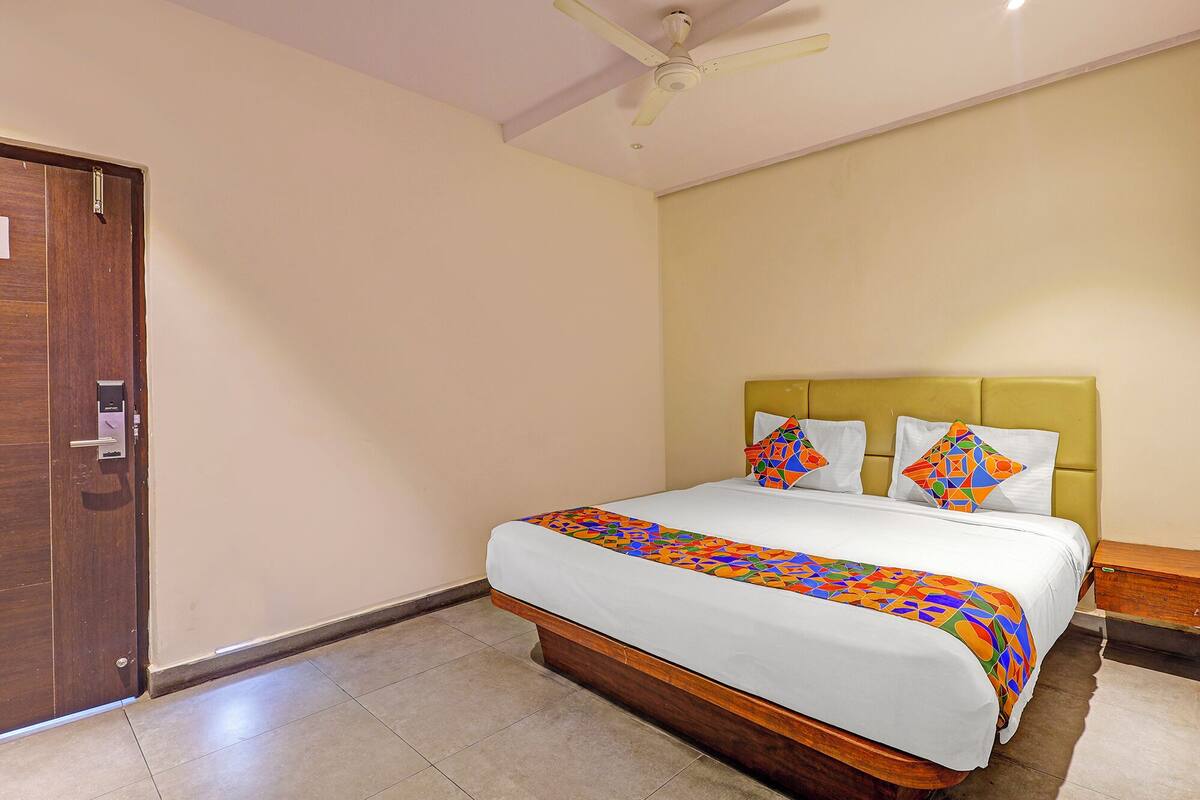 A hotel room with a bed, a wooden door, a ceiling fan, and a nightstand.