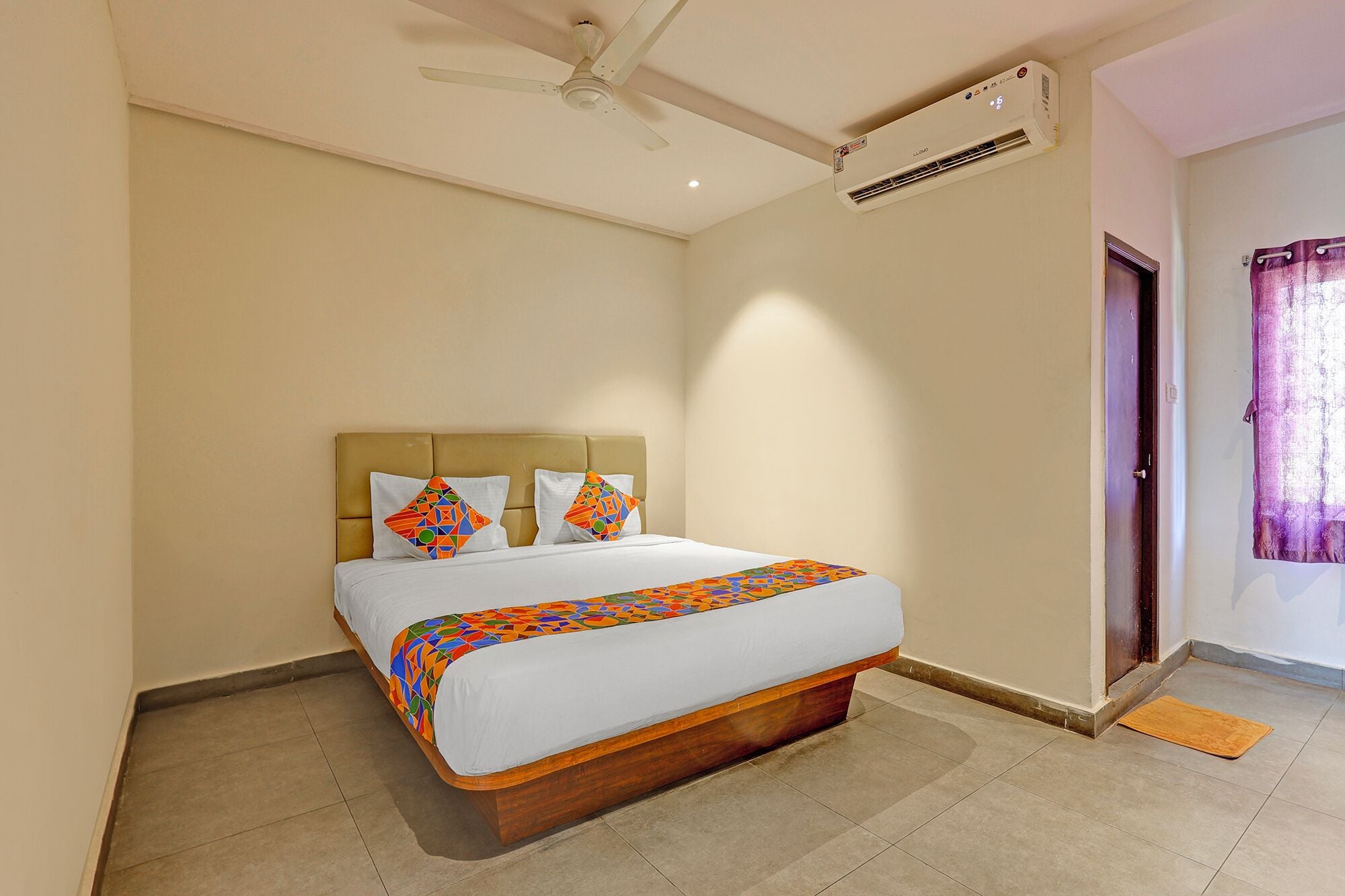 A bedroom with a bed, a ceiling fan, an air conditioning unit, a door, and a window with curtains.