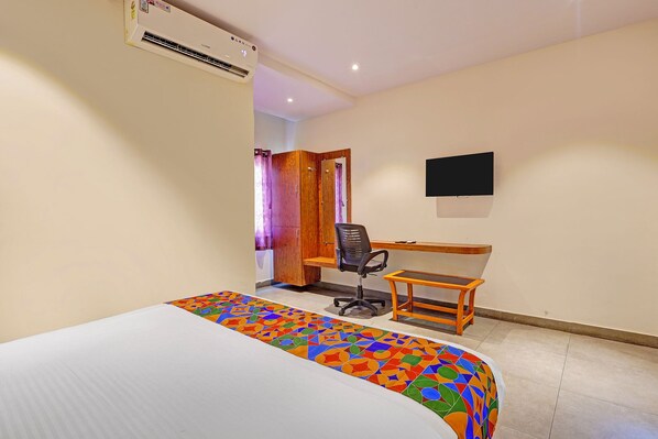 A hotel room with a bed, a desk, a chair, an air conditioning unit, and a television. - Fabhotel Siddarth Grand (Vijayawada)