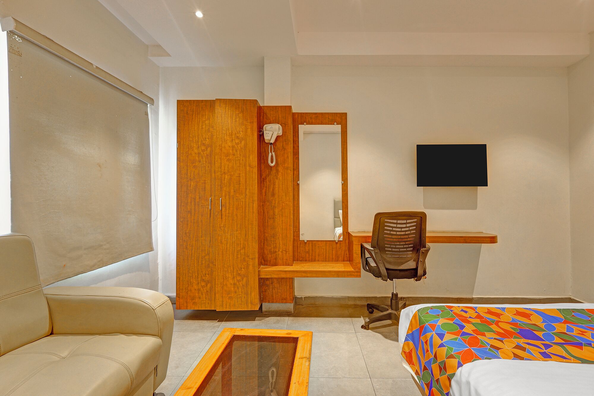 A bedroom with a bed, a desk with a chair, a wardrobe, a television, and a window.