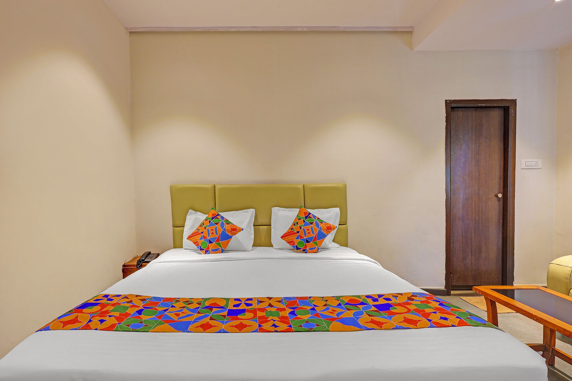 Una habitación de hotel con una cama, dos almohadas, una mesita de noche y una puerta de madera.