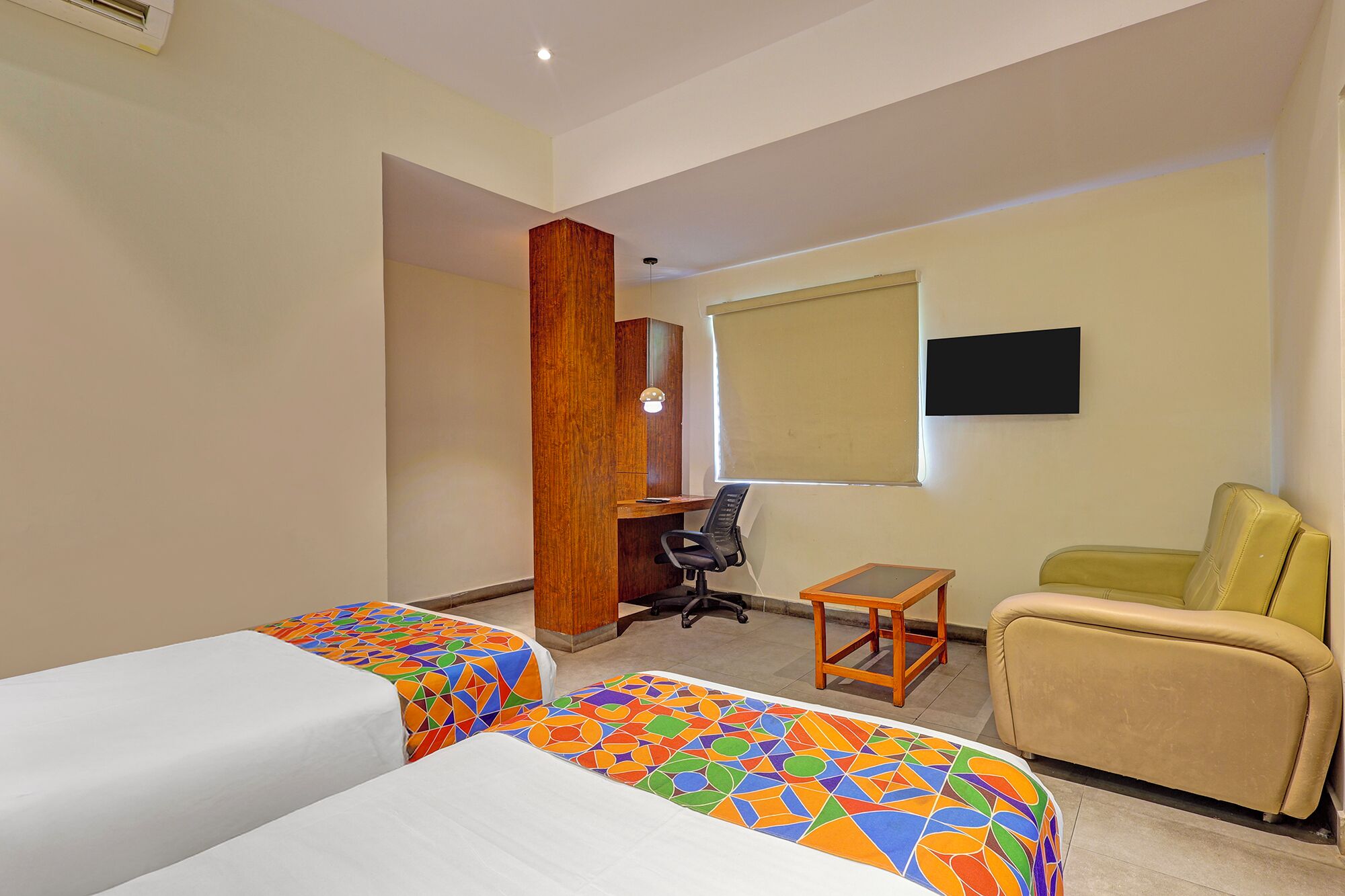 A hotel room with two beds, a desk, a chair, and a TV.