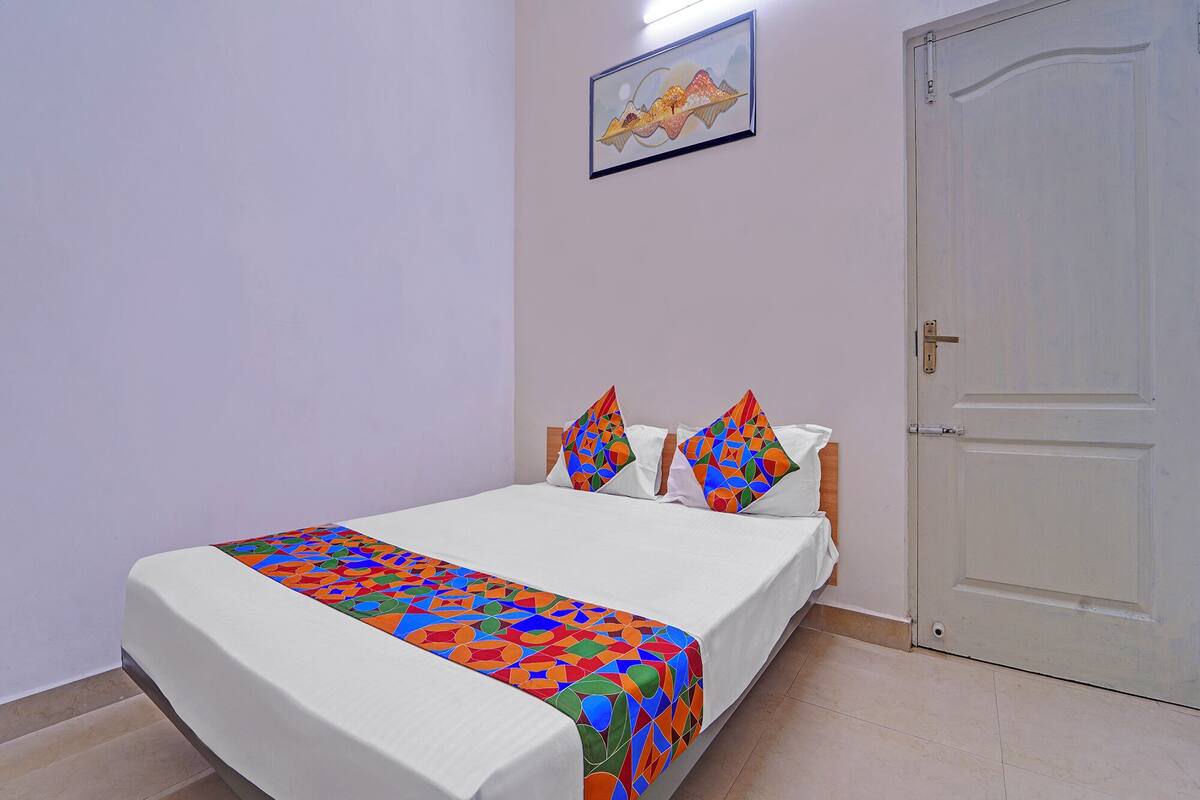 Ein ordentlich bezogenes Bett mit einer farbenfrohen Bettdecke mit geometrischem Muster, Kissen, einer schlichten weißen Wand und einer geschlossenen Tür.