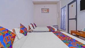 A hotel room with two beds, a small table, a door, and a window with curtains.