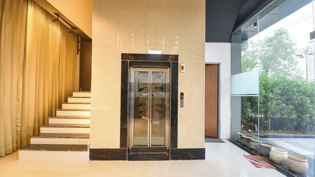 A modern hotel lobby with a marble staircase, a glass elevator, and a view of greenery outside. - Fabhotel Sky I (Gurugram)