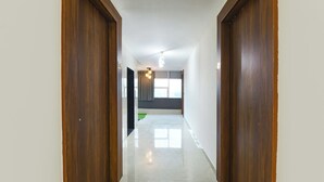 A hallway with wooden doors, a tiled floor, and a view into a room with a window and curtains. - Fabhotel Sky I (Gurugram)