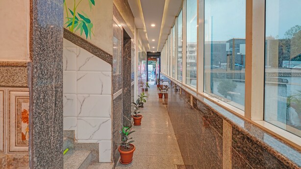 A corridor with marble walls, potted plants, and large windows. - Fabhotel Sapthagiri Suites Inn (Bengaluru)