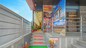 A hotel entrance with multiple steps leading up to a green mat, potted plants, and signs indicating available rooms. - Fabhotel Sapthagiri Suites Inn (Bengaluru)