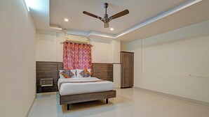 A bedroom with a bed, a ceiling fan, a wardrobe, and a window with curtains. - Fabhotel Sapthagiri Suites Inn (Bengaluru)
