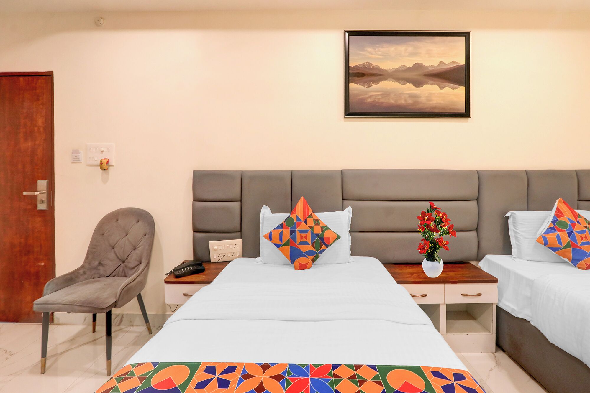 A hotel room with a large bed, two bedside tables, a chair, a painting on the wall, and a vase with flowers.