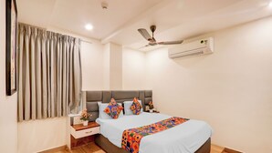 A bedroom with a bed, nightstand, wall-mounted air conditioner, ceiling fan, and a window with curtains. - Fabhotel Radha Rani Residency (Khammam)