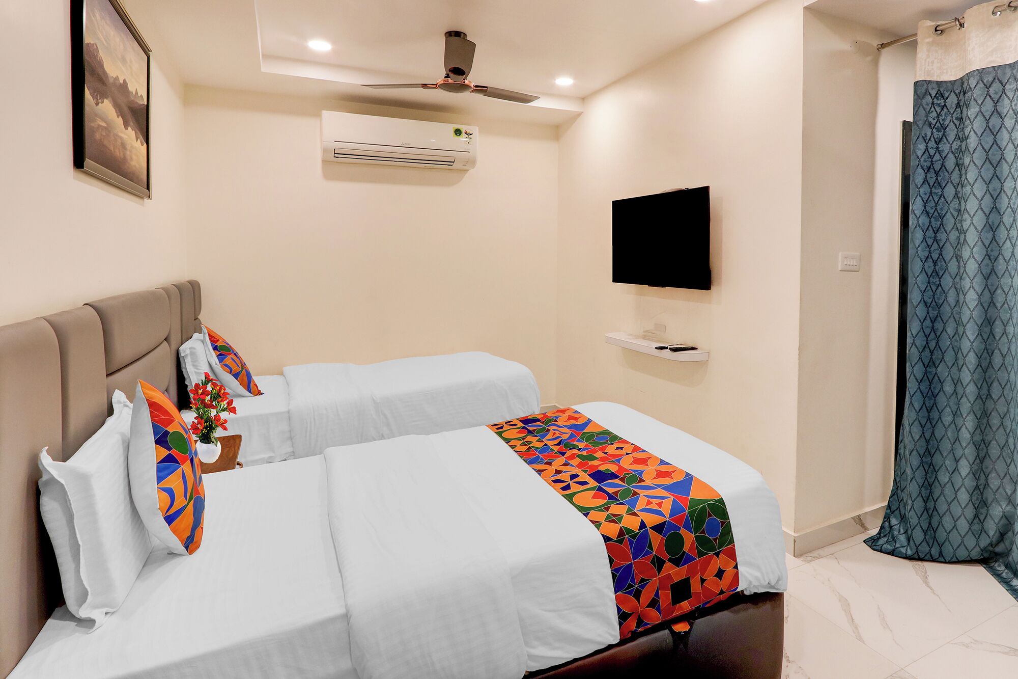 A hotel room with two beds, a ceiling fan, an air conditioning unit, a flat-screen TV, and a shower area with a curtain.