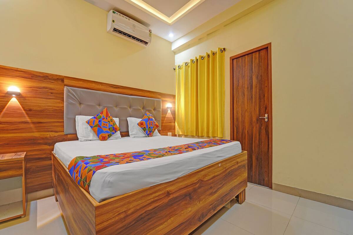 A bedroom with a wooden bed, a headboard, a nightstand, a wall-mounted air conditioner, and a yellow curtain.