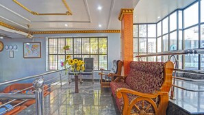 A lobby with a marble floor, a wooden bench with a wheel, a black leather chair, a vase with sunflowers, and a world map on the wall. - Fabhotel Amutham Residency (Kanyakumari)