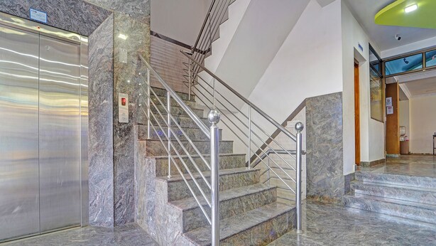 A modern interior with a marble staircase, metal railings, and a digital elevator display. - Fabhotel Amutham Residency (Kanyakumari)
