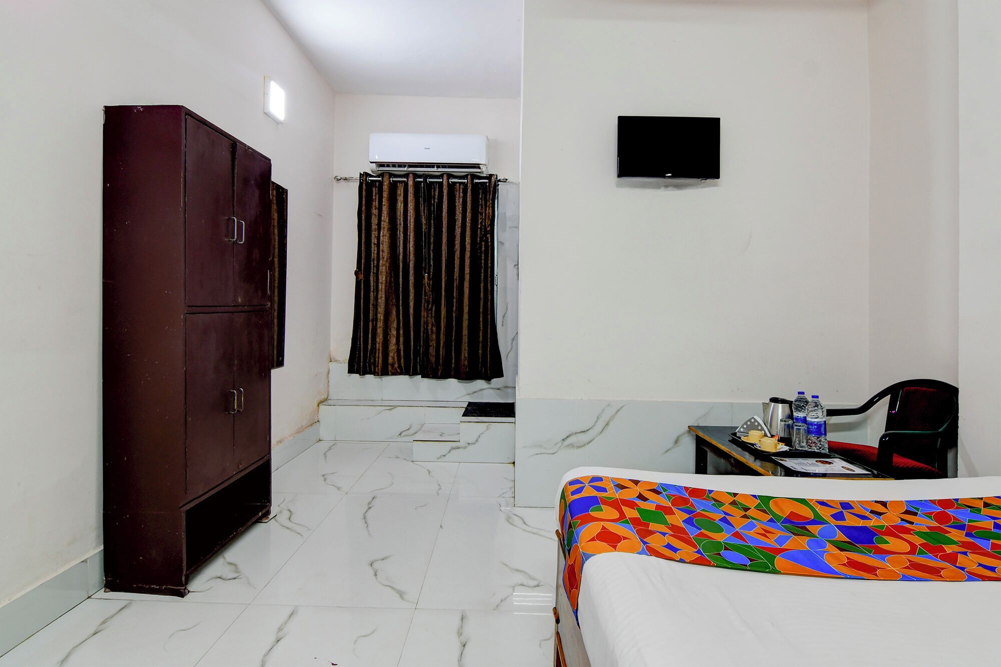 Une chambre d’hôtel comprenant un lit, un bureau avec une chaise, une armoire, un rideau de douche et un téléviseur fixé au mur.