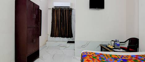 A hotel room with a bed, a desk with a chair, a wardrobe, a shower curtain, and a television on the wall.