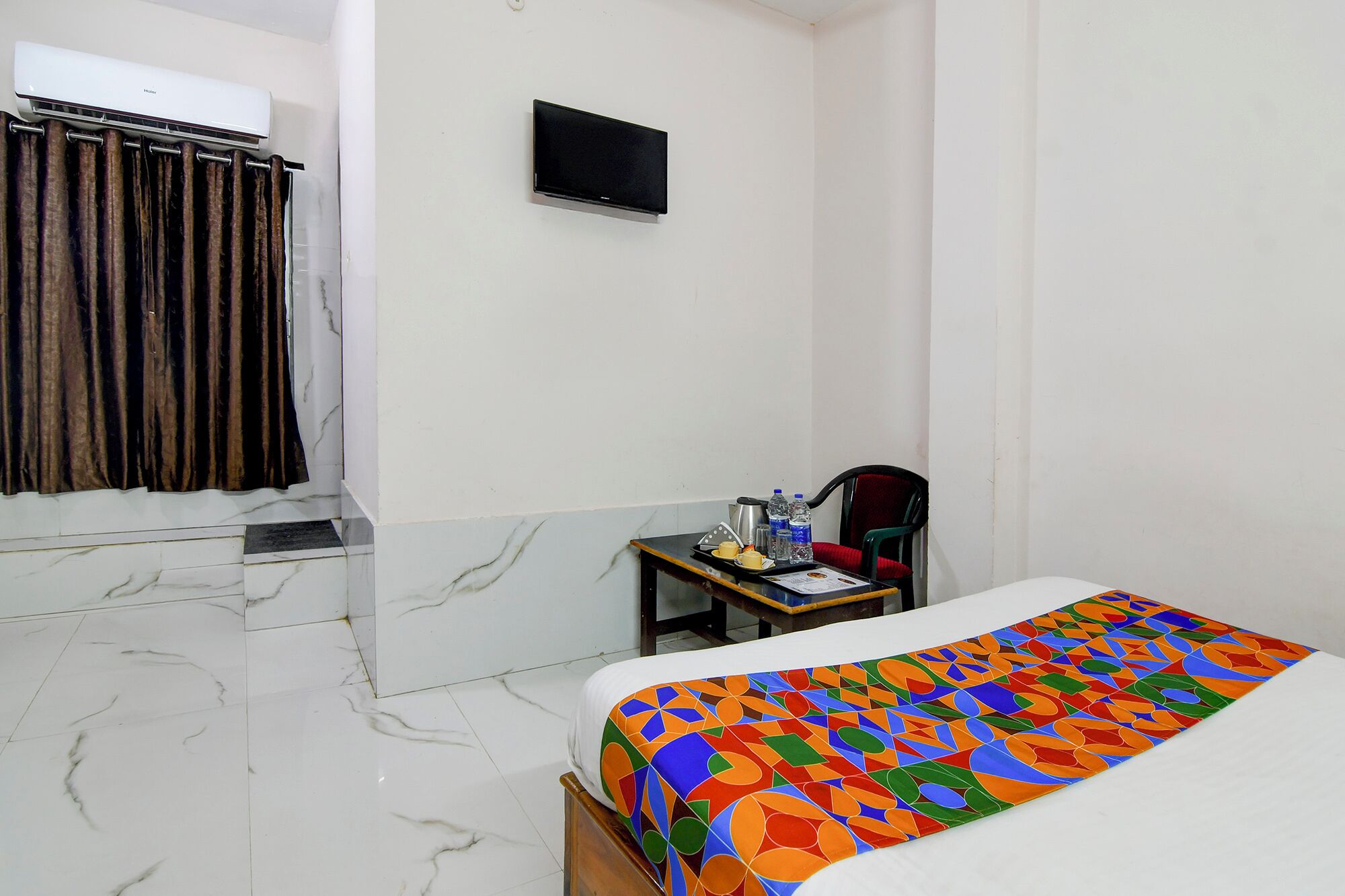 A hotel room with a bed, a desk, a chair, a TV, and a bathroom with a shower curtain.