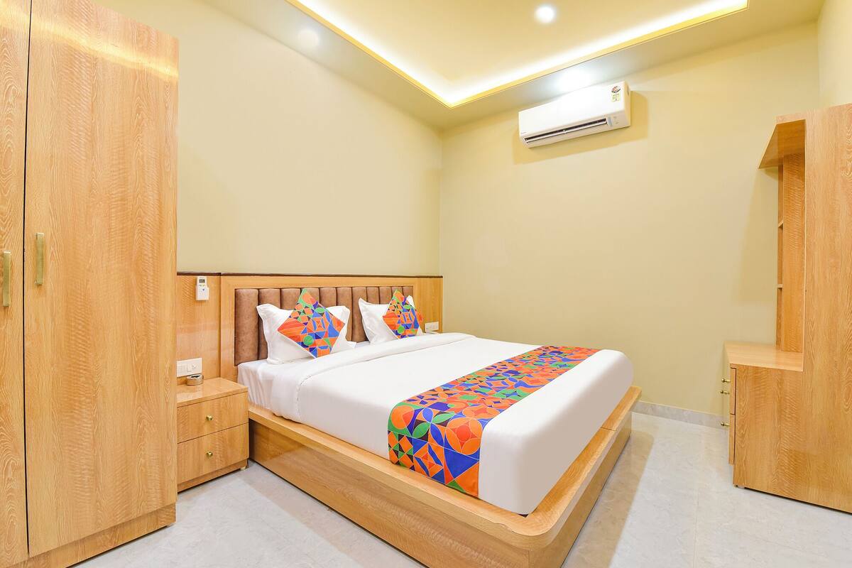A hotel room with a wooden bed frame, a bedside table, a wardrobe, and an air conditioning unit.