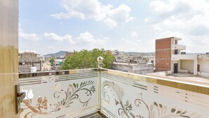 Un balcon agrémenté de panneaux de verre décoratifs, offrant une vue sur un paysage urbain avec des bâtiments et un arbre.
