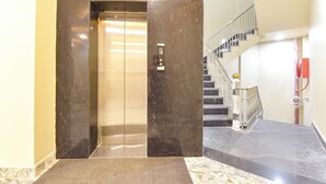 Un ascenseur aux finitions métalliques et doté d’un panneau de commande, qui mène à un escalier avec une rampe métallique et un tuyau d’incendie rouge.