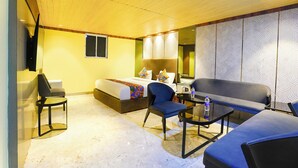 A hotel room with a bed, a desk, a chair, a sofa, and a small table with a bottle. - Fabhotel Nexus Inn (Mumbai)