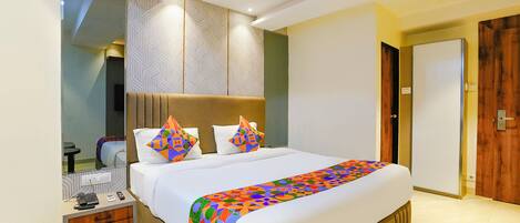 A hotel room with a large bed, a bedside table with a phone and charger, a mirror, and a door to the right.