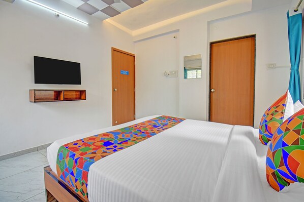 A hotel room with a bed, a television mounted on the wall, two doors, and a window with curtains. - Fabhotel Shree Krishna Inn (Pune)