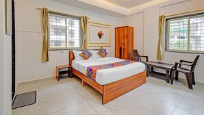 Quarto de hotel com uma cama grande, um guarda-roupa de madeira, uma secretária e duas cadeiras.