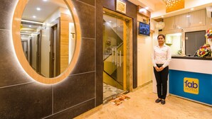 A hotel reception area with a modern design, including a large mirror, a reception desk with the hotel logo, and a staircase leading to other floors. - Fabhotel Hill Fort (Kolkata)