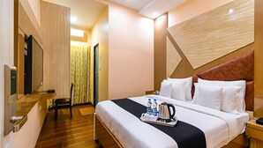 A hotel room with a bed, a bedside table, a TV, and a wooden floor. - Fabhotel Hill Fort (Kolkata)