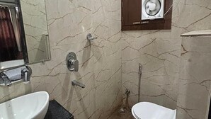 A bathroom with a marble wall, a sink, a toilet, and a shower. - Fabhotel Rk Retreat (Bhopal)