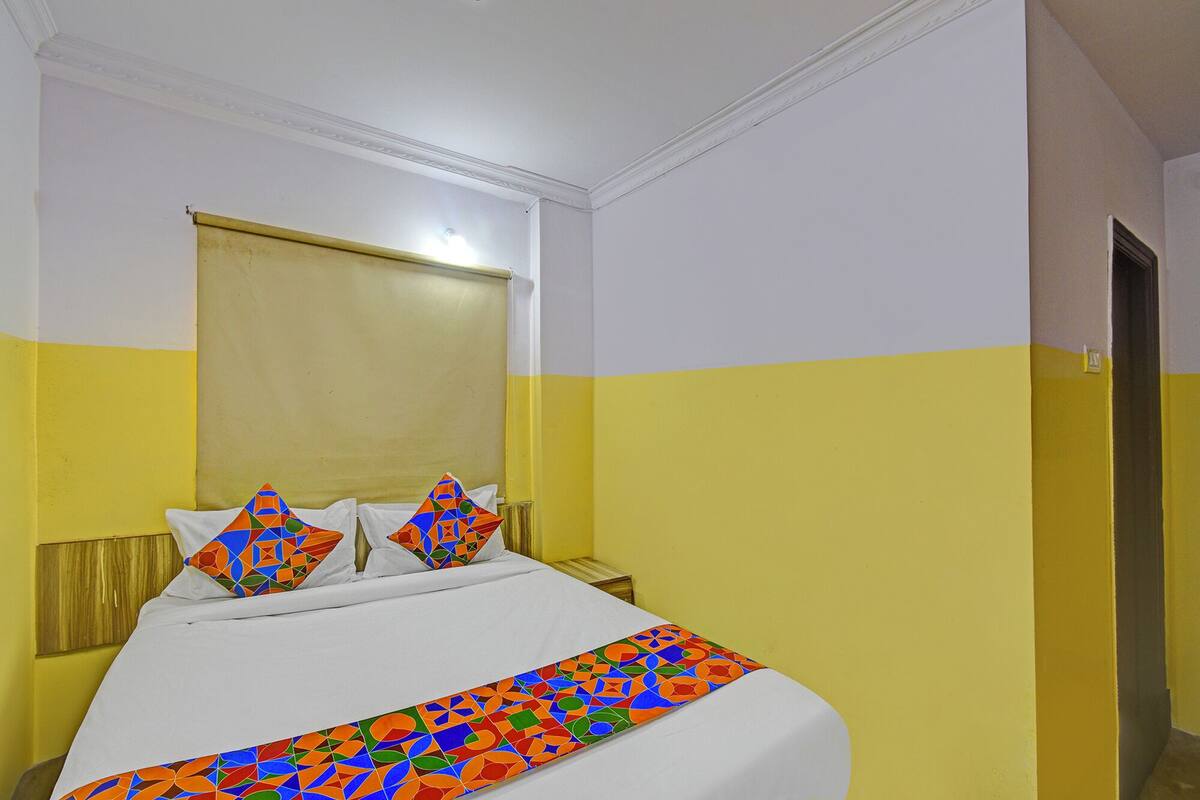 Une chambre d’hôtel avec un lit, du linge de lit blanc, une couvre-lit aux motifs géométriques colorés et des murs jaunes.