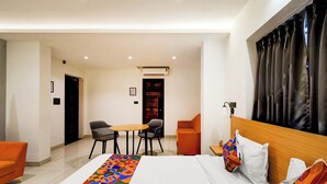 A hotel room with a bed, a small table with chairs, a sofa, and a window with curtains. - Fabhotel Casa Grand (Hyderabad)