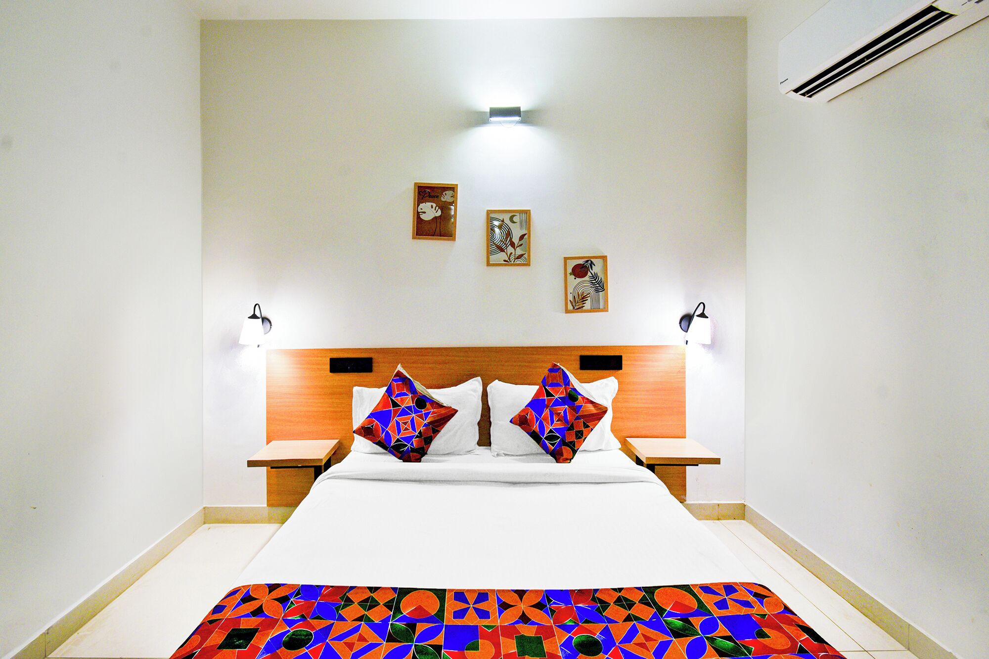 A hotel room with a large bed, two bedside tables, and a nightstand. There are three wall-mounted artworks above the bed.