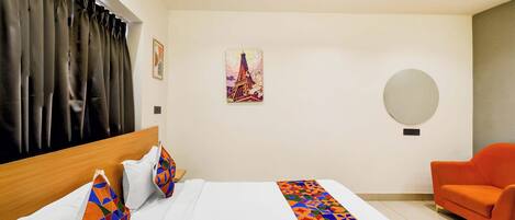 Una habitación de hotel con una cama, una silla, un cuadro y un espejo redondo en la pared.