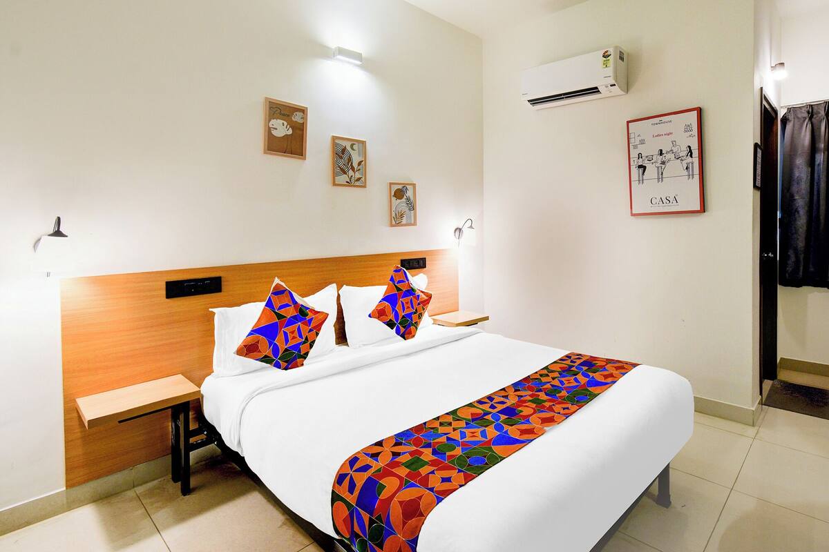 Una habitació d'hotel amb un llit, una tauleta de nit, aire condicionat fixat a la paret i un quadre encimbellat.