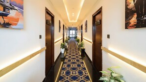 A hotel hallway with a patterned carpet, wooden doors, and framed artwork on the walls. - Fabhotel Casa Grand (Hyderabad)