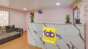 A reception desk with a marble top and a logo for 'fab hotels'. There is a sofa with a floral cushion and a potted plant on the desk. - Fabhotel The Heaven (Pune)