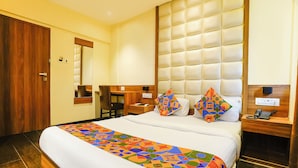 A hotel room with a large bed, a wooden desk, a chair, a mirror, and a wall-mounted TV. - Fabhotel Ratna Mahal (Mumbai)