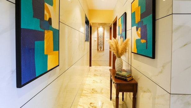 A hallway with marble flooring, abstract paintings on the walls, and a vase with dried plants on a wooden table. - Fabhotel Ratna Mahal (Mumbai)