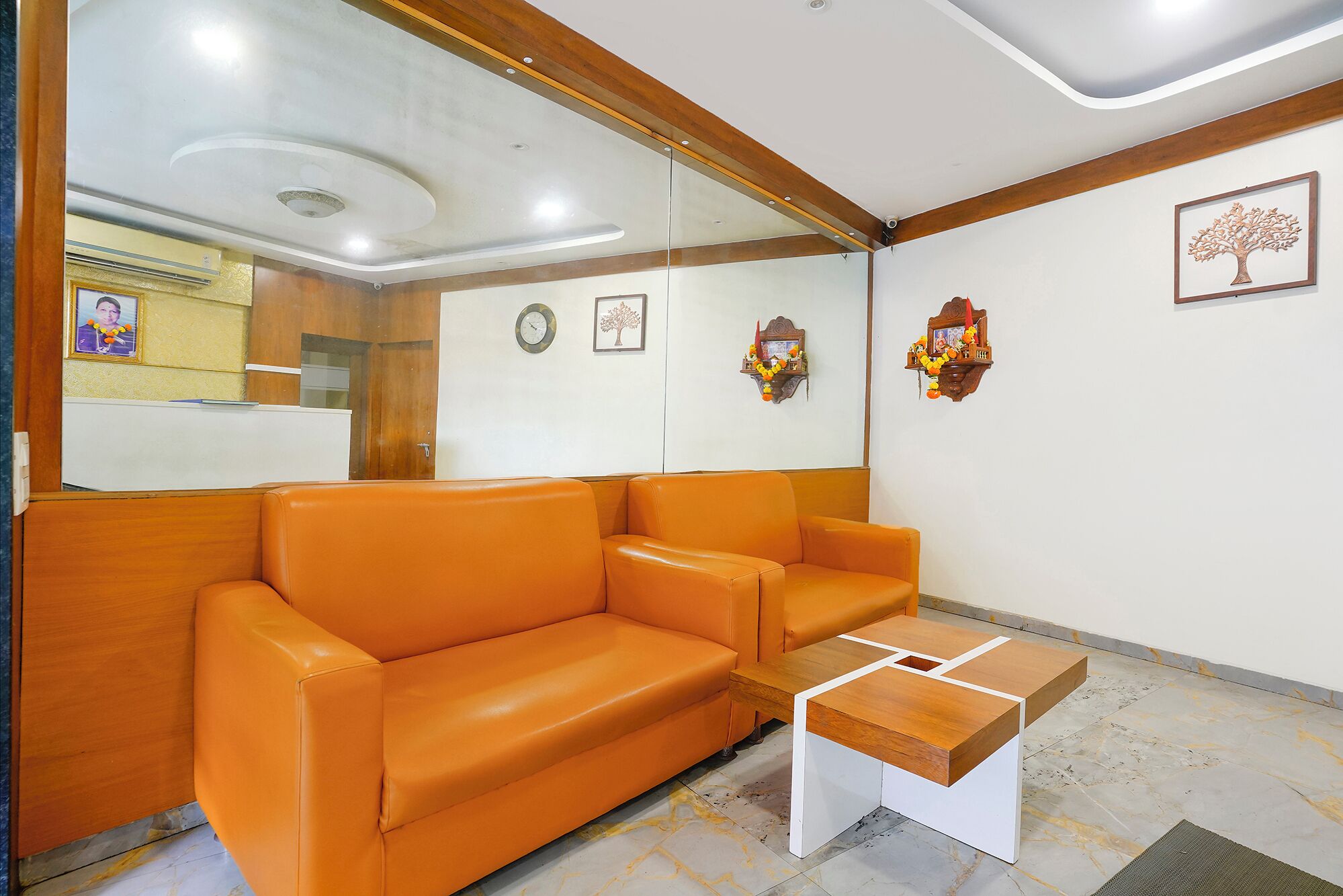 A reception area with a wooden reception desk, an orange leather sofa, a wall clock, and a framed picture of a tree.