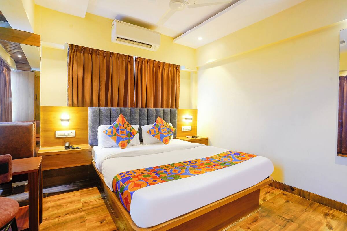 A hotel room with a bed, bedside lamps, an air conditioner, and a wooden floor.