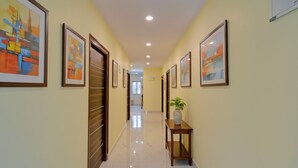 A hallway with framed artwork on the walls, a marble floor, and a wooden door. - Fabhotel Srikara Grand Luxury Rooms (Hyderabad)