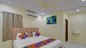 A hotel room with a bed, a ceiling fan, an air conditioning unit, a wall-mounted TV, and a bathroom with a sink and mirror. - Fabhotel Srikara Grand Luxury Rooms (Hyderabad)